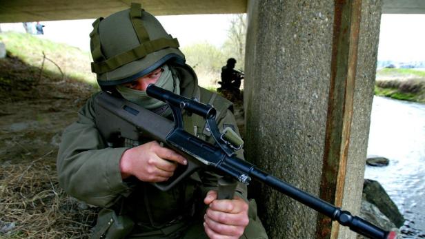 Ein Soldat mit Helm und Gewehr kauert unter einer Brücke.