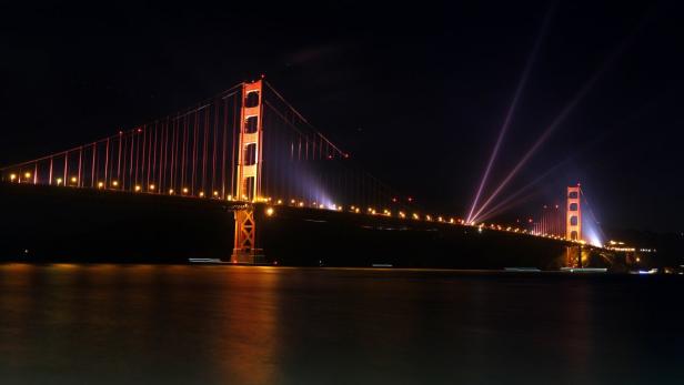 Die Golden Gate Bridge in der Nacht, beleuchtet mit Scheinwerfern.