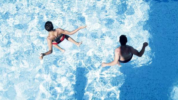 Zwei Männer schwimmen in einem hellblauen Schwimmbad.