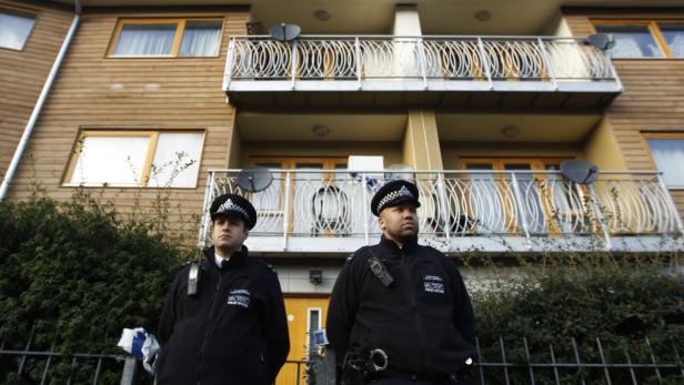Zwei Polizisten stehen vor einem Wohnhaus mit Balkonen.
