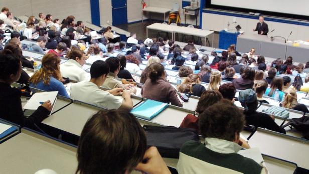 Ein Dozent hält einen Vortrag vor einem großen Publikum in einem Hörsaal.