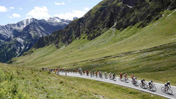 Eine Gruppe Radfahrer fährt eine Straße entlang in einer grünen Berglandschaft.