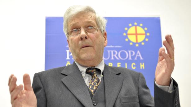 Ein Mann mit Brille gestikuliert vor einem Banner mit der Aufschrift „Europa Reich“.