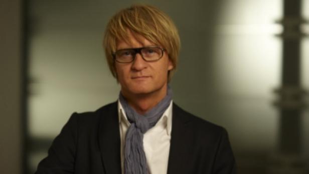 Ein Mann mit blonden Haaren, Brille und Schal blickt in die Kamera.