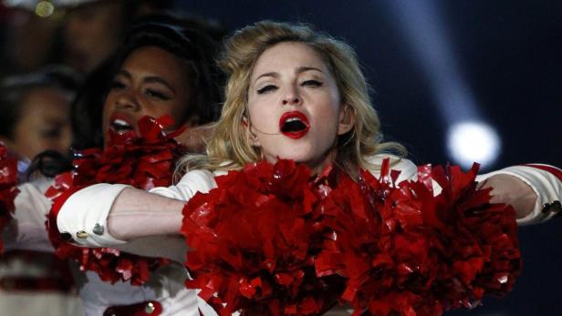 Madonna tritt mit Cheerleadern und roten Pompons auf einer Bühne auf.