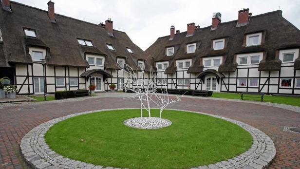 Ein Hotel mit Reetdach und einem kleinen Kreisverkehr mit Bäumen im Vorgarten.