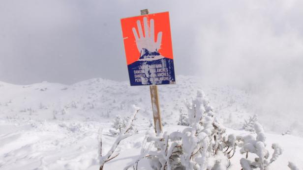 Ein Lawinengefahr-Schild steht in einer verschneiten Berglandschaft.