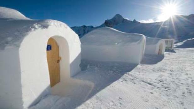 Eine Reihe von Iglus vor einer verschneiten Bergkulisse unter strahlendem Sonnenschein.