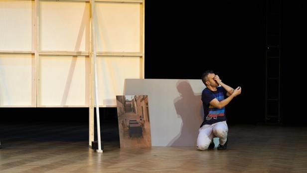 Ein Mann kniet auf einer Bühne neben Requisiten und einer Fotografie.