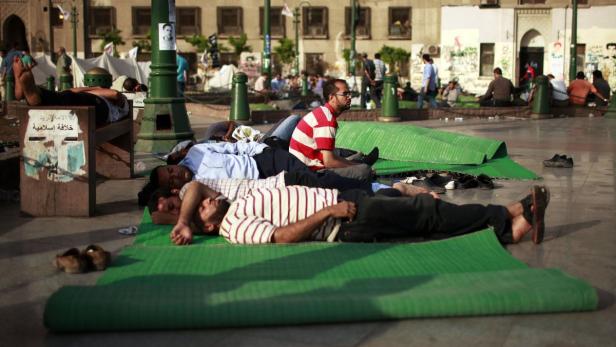 Mehrere Männer ruhen sich auf Matten in einem städtischen Gebiet aus.
