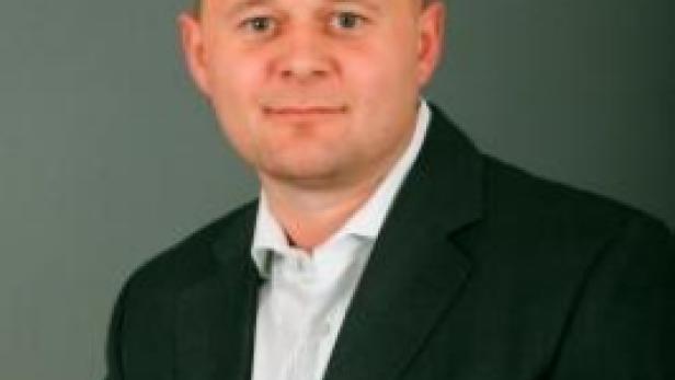 Ein Mann mit Anzug und Hemd vor einem grauen Hintergrund.