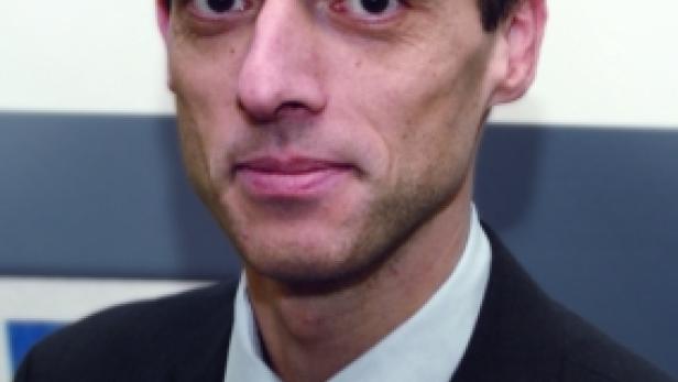 Ein Mann im Anzug mit Krawatte vor einem unscharfen Hintergrund.