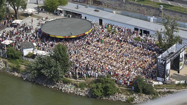 Eine große Menschenmenge versammelt sich am Ufer eines Flusses für eine Veranstaltung.
