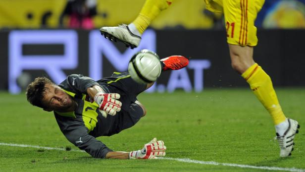 Ein Fußballspieler tritt einen Ball, während ein Torwart versucht, ihn abzuwehren.
