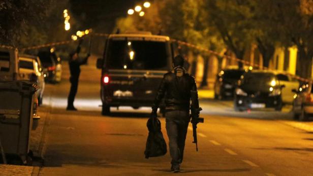 Ein Mann geht nachts mit einem Gewehr und einer Tasche auf einer abgesperrten Straße entlang.