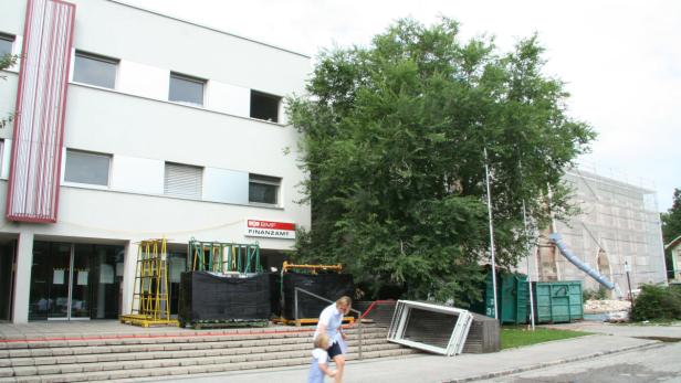 Eine Frau geht mit einem Kind vor einem Gebäude des BMF Finanzamt vorbei.