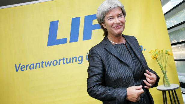 Eine Frau in einem dunklen Blazer posiert vor einem gelben Banner der Partei LIF.