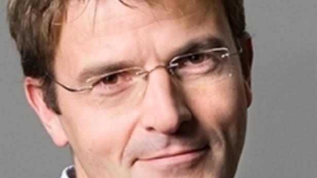 Ein Mann mit Brille und Anzug blickt in die Kamera.