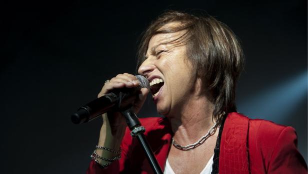 Eine Sängerin mit rotem Blazer singt in ein Mikrofon.