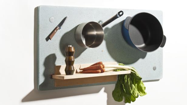 Ein Messer, Töpfe, Karotten und Mangold hängen an einer Küchenwand.