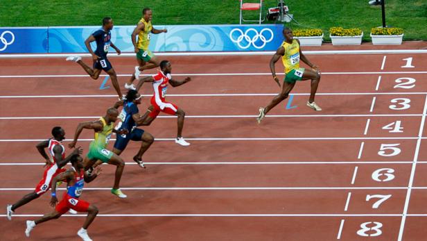 Mehrere Sprinter laufen auf einer roten Bahn bei einem Leichtathletikwettbewerb.