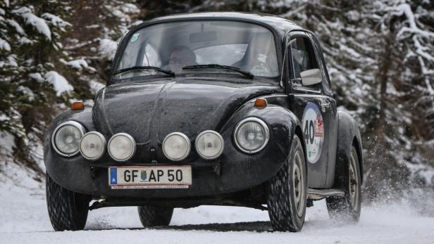 Ein schwarzer VW Käfer fährt auf einer schneebedeckten Straße.