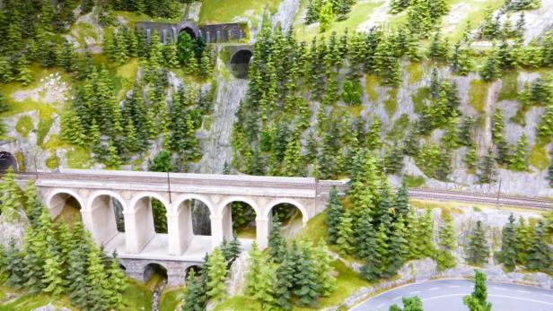 Eine Miniaturlandschaft mit Bergen, Tunnels, einer Eisenbahnbrücke und einer gewundenen Straße.