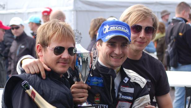 Drei Männer posieren mit einer Trophäe und einer Champagnerflasche.