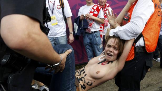 Eine Frau mit aufgemaltem Text auf dem Körper wird von Polizisten abgeführt.