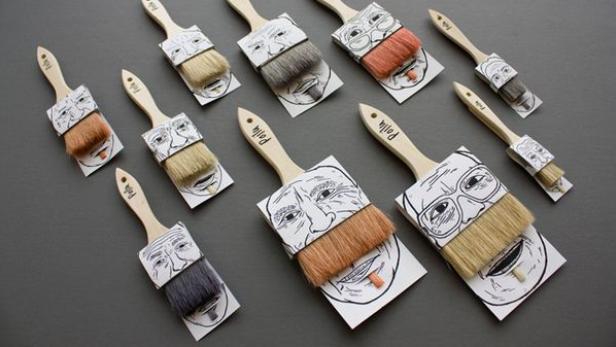 Mehrere Pinsel mit aufgedruckten Gesichtern liegen auf einem grauen Untergrund.