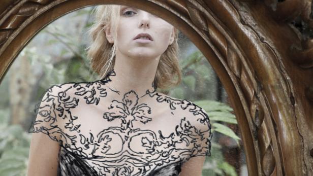 Eine Frau mit blonden Haaren blickt in einen verzierten Spiegel.