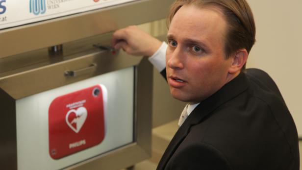 Ein Mann in Anzug öffnet einen AED-Schrank mit einem Philips-Defibrillator.