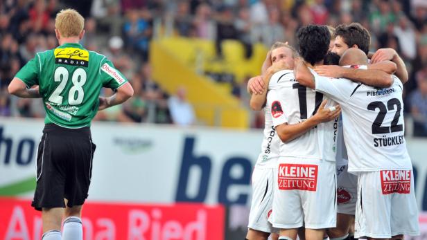 Fußballspieler umarmen sich auf dem Spielfeld, während ein anderer Spieler daneben steht.