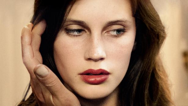 Das Porträt einer Frau mit roten Lippen und einer Hand an ihrer Wange.