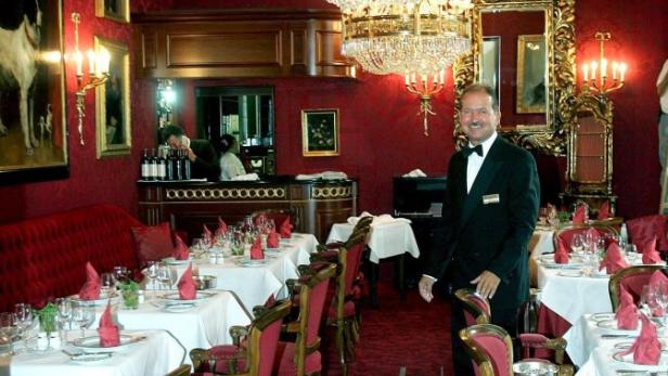 Ein Kellner steht in einem eleganten Restaurant mit roter Dekoration und Kronleuchtern.