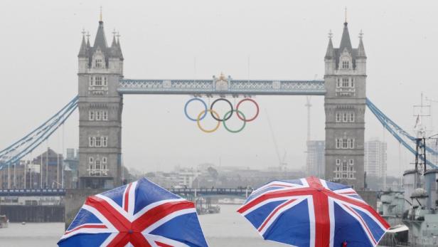Two tourists stand under Union flag umbrellas as they take pictures from London Bridge, of Tower Bridge adorned with the Olympic rings, on a wet summers morning in central London July 6, 2012. Many parts of Britain are due to receive an average months rai