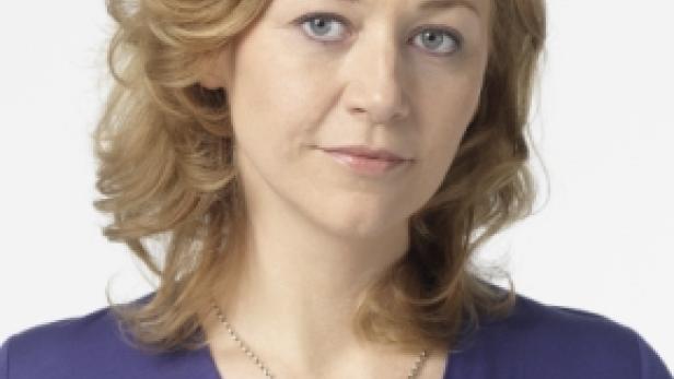 Porträt einer Frau mit blonden, gewellten Haaren und einem lila Oberteil.