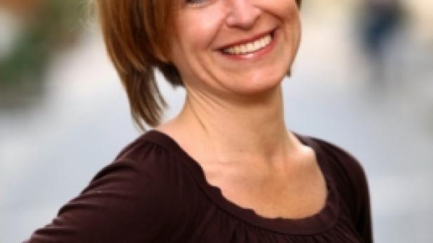 Eine lächelnde Frau mit braunem Oberteil posiert im Freien.