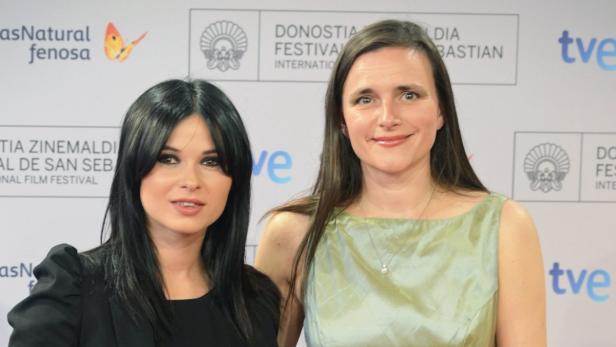 Zwei Frauen posieren vor einem Banner des San Sebastián International Film Festivals.