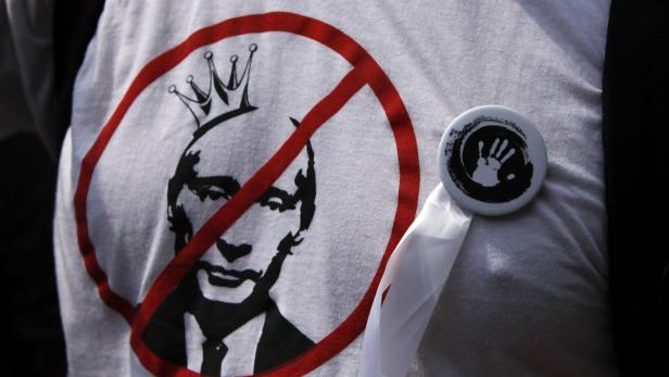 Ein T-Shirt mit einem durchgestrichenen Porträt von Putin mit Krone und einem Button mit Handabdruck.