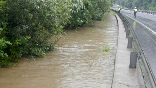 Hochwasser hat eine Straße überflutet, zwei Personen in Warnwesten stehen am Rand.