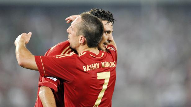 Zwei Fußballspieler von Bayern München umarmen sich auf dem Spielfeld.