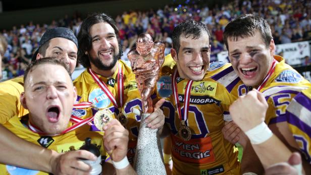 Eine Gruppe American-Football-Spieler feiert mit einer Trophäe ihren Sieg.