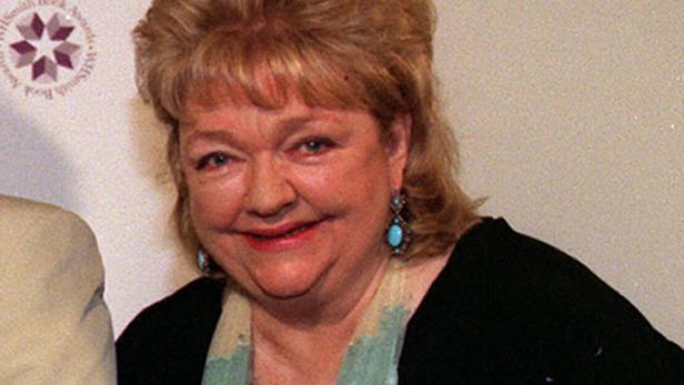 Eine lächelnde Frau mit blonden Haaren und türkisfarbenen Ohrringen.