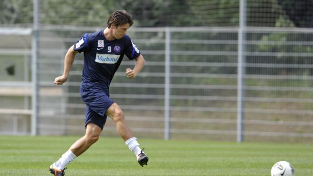 Ein Fußballspieler in blau-violetter Sportkleidung dribbelt einen Ball auf einem grünen Rasen.