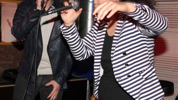 Ein Mann und eine Frau singen in einer Bar in Mikrofone.