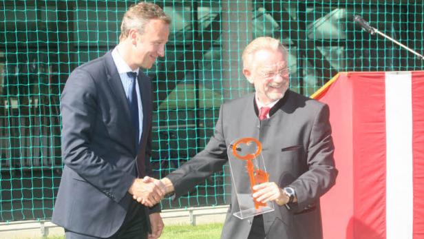 Zwei Männer im Anzug schütteln sich die Hände, einer hält einen übergroßen Schlüssel.