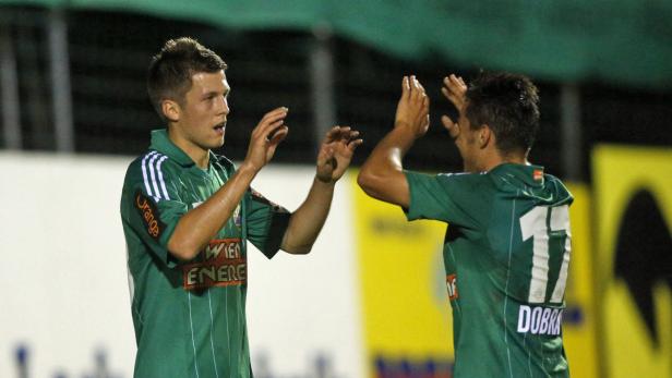 Zwei Fußballspieler in grünen Trikots feiern gemeinsam auf dem Spielfeld.
