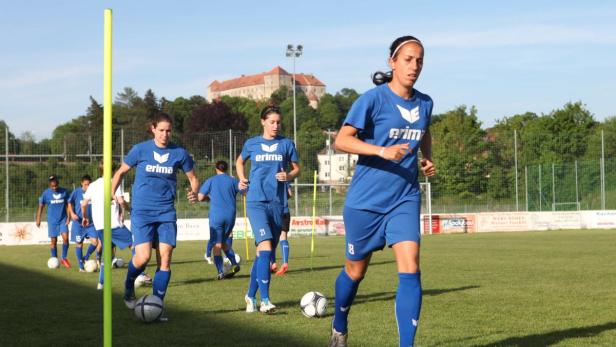 Eine Gruppe von Fußballspielerinnen trainiert auf einem Rasenplatz vor einem Schloss.