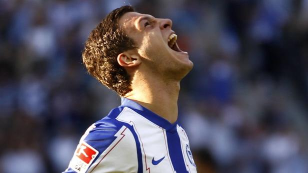 Ein Fußballspieler in einem weißen und blauen Trikot jubelt mit geöffnetem Mund.